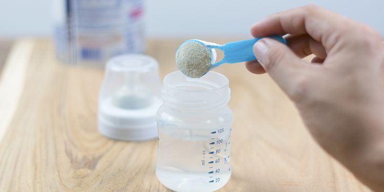 Powder milk and blue spoon on light background close up. Milk powder for baby in measuring spoon on can. Powdered milk with spoon for baby. Baby Milk Formula and Baby Bottles.